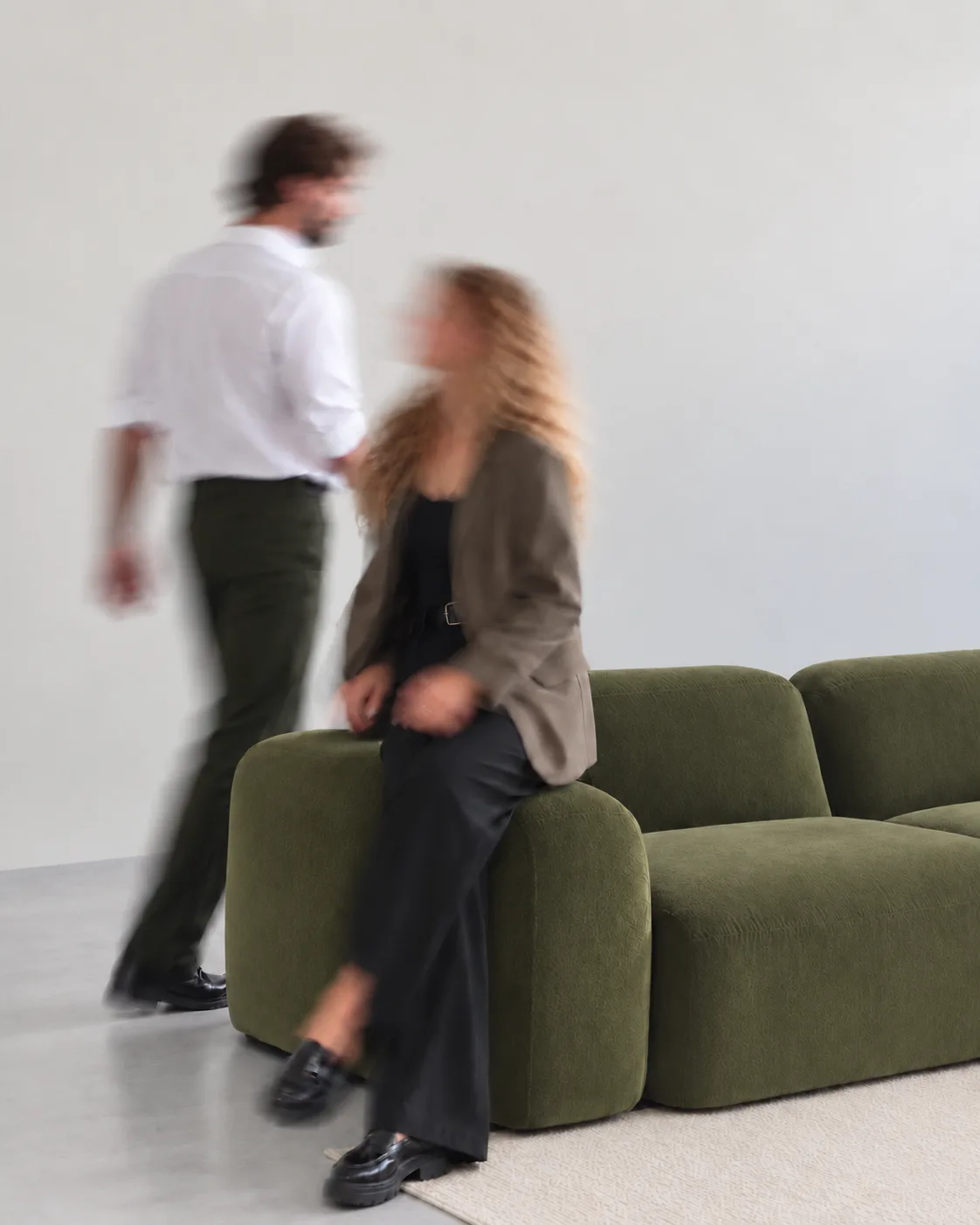 Two people talking next to an olive-green sofa in a bright room